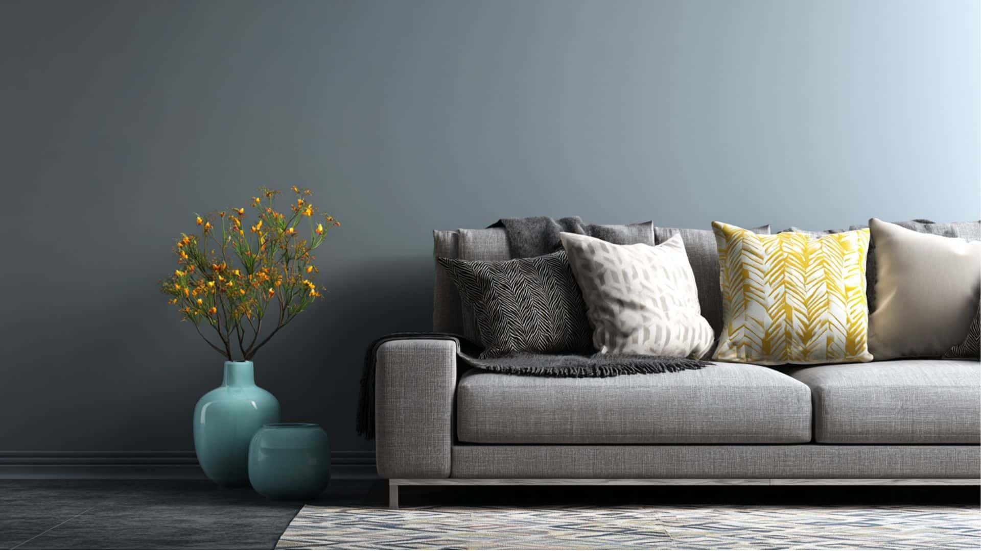 Gray sofa with patterned cushions beside blue vases holding yellow flowers, set against a muted wall in a modern living room.