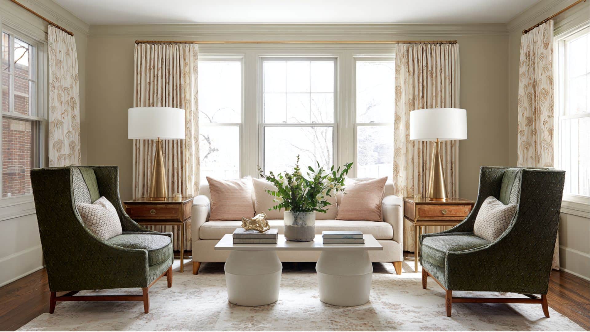 Elegant living room with a beige sofa, green chairs, a central coffee table, and large windows framed by patterned curtains