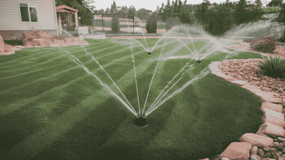A well-maintained lawn with sprinkler systems watering the grass, surrounded by rocks and a neat landscape.