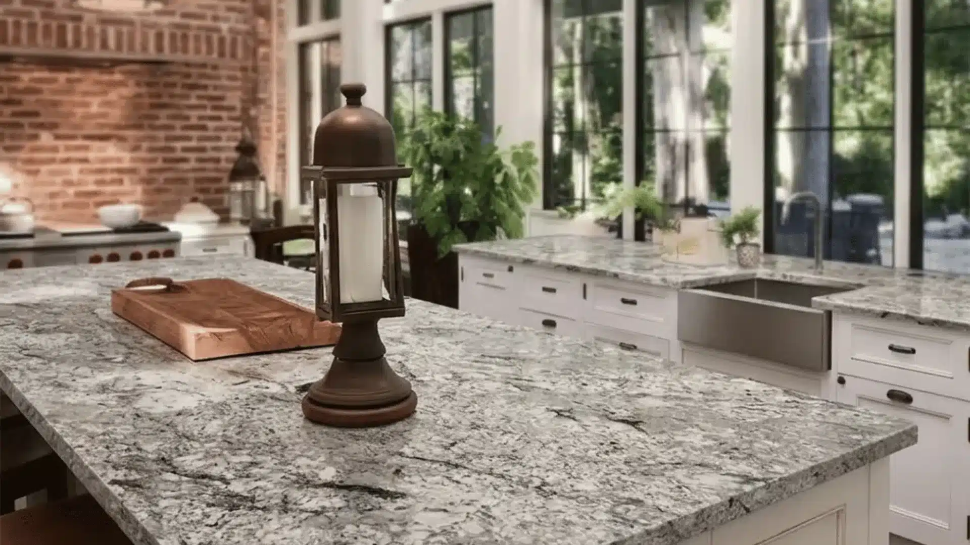 bright kitchen with white cabinets, granite island, brick wall, pendant lights, and windows with trees