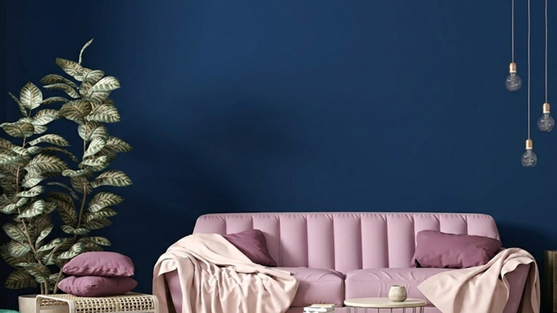 chic modern living room featuring a pink channeled sofa, wooden furniture, an indoor plant, and hanging bulbs against a dark blue matte wall