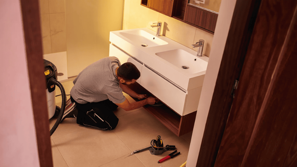 construction worker repairing a white bathroom vanity with tools on the floor in a modern bathroom