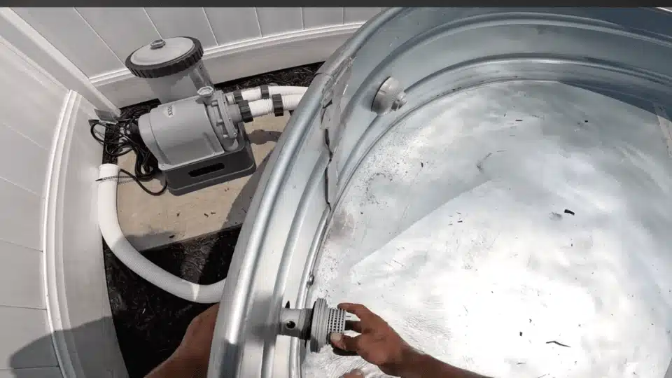 hands installing a plastic outlet strainer fitting into the side of a galvanized stock tank pool