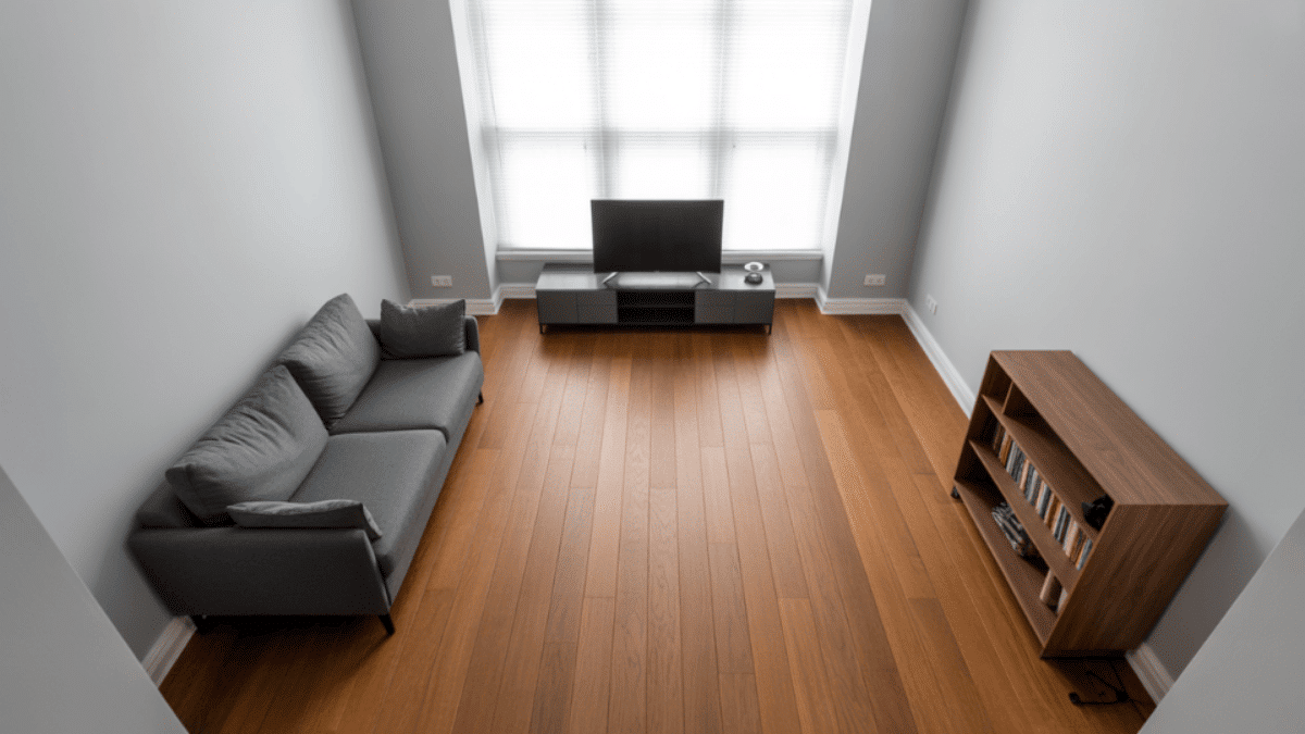 overhead view of a minimal living room with warm wood floor dominating the space and sparse furniture at the edges