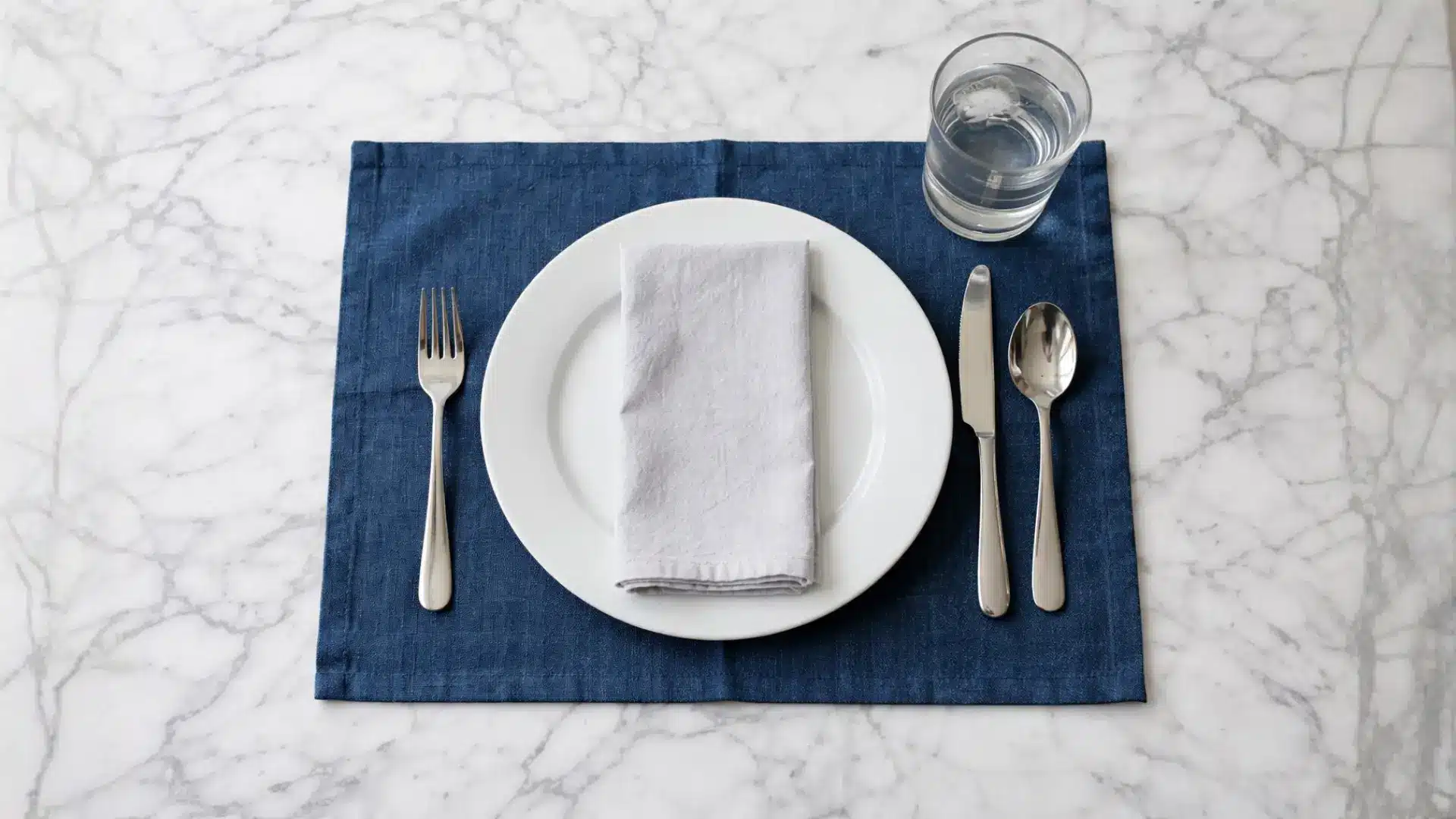 the basic table setting for everyday meals shows a plate, napkin, fork, knife, spoon, and glass on a blue placemat