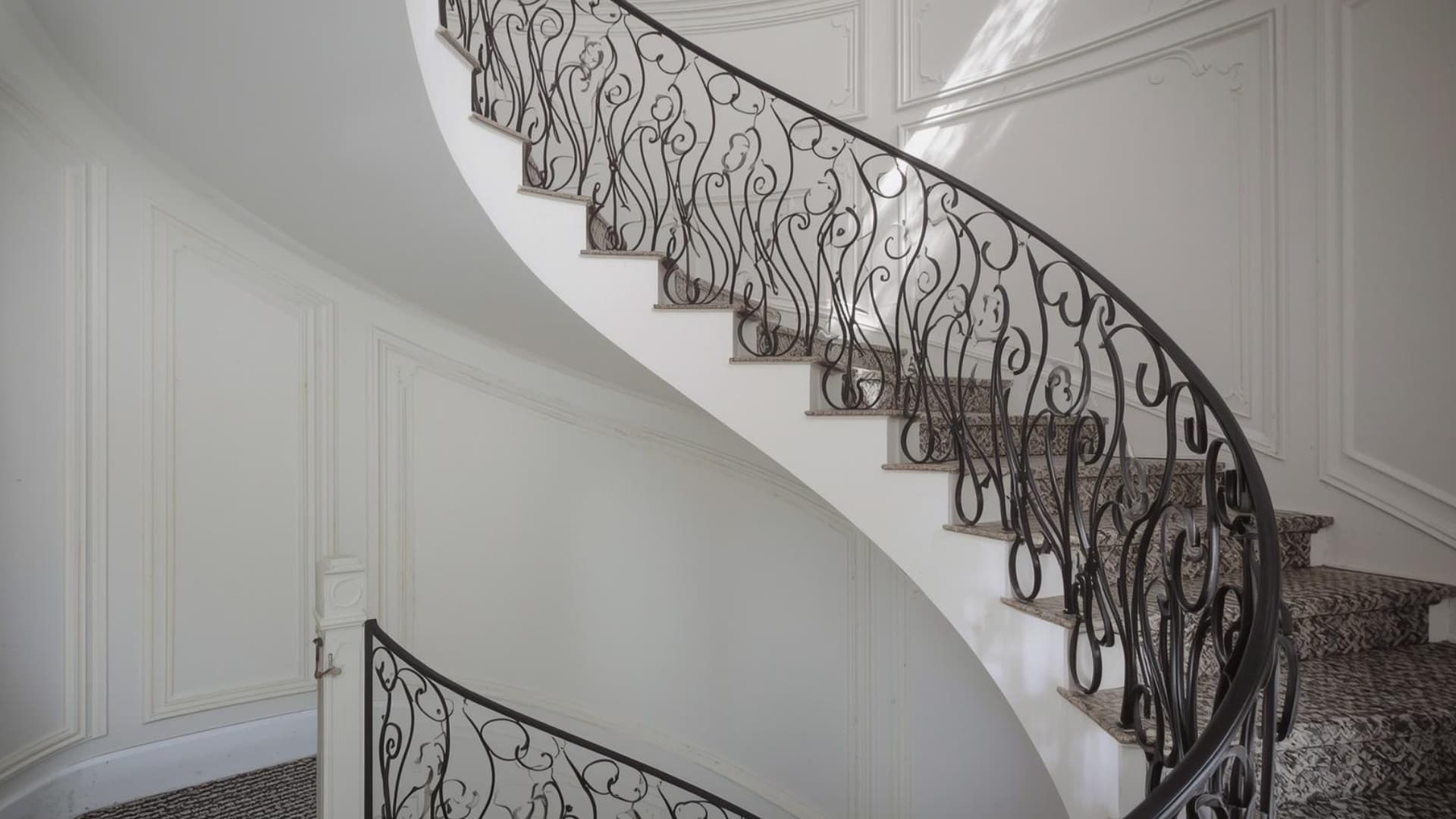 white winding staircase with intricate wrought iron scrolling banisters against classic paneled walls in a bright, sophisticated interior space