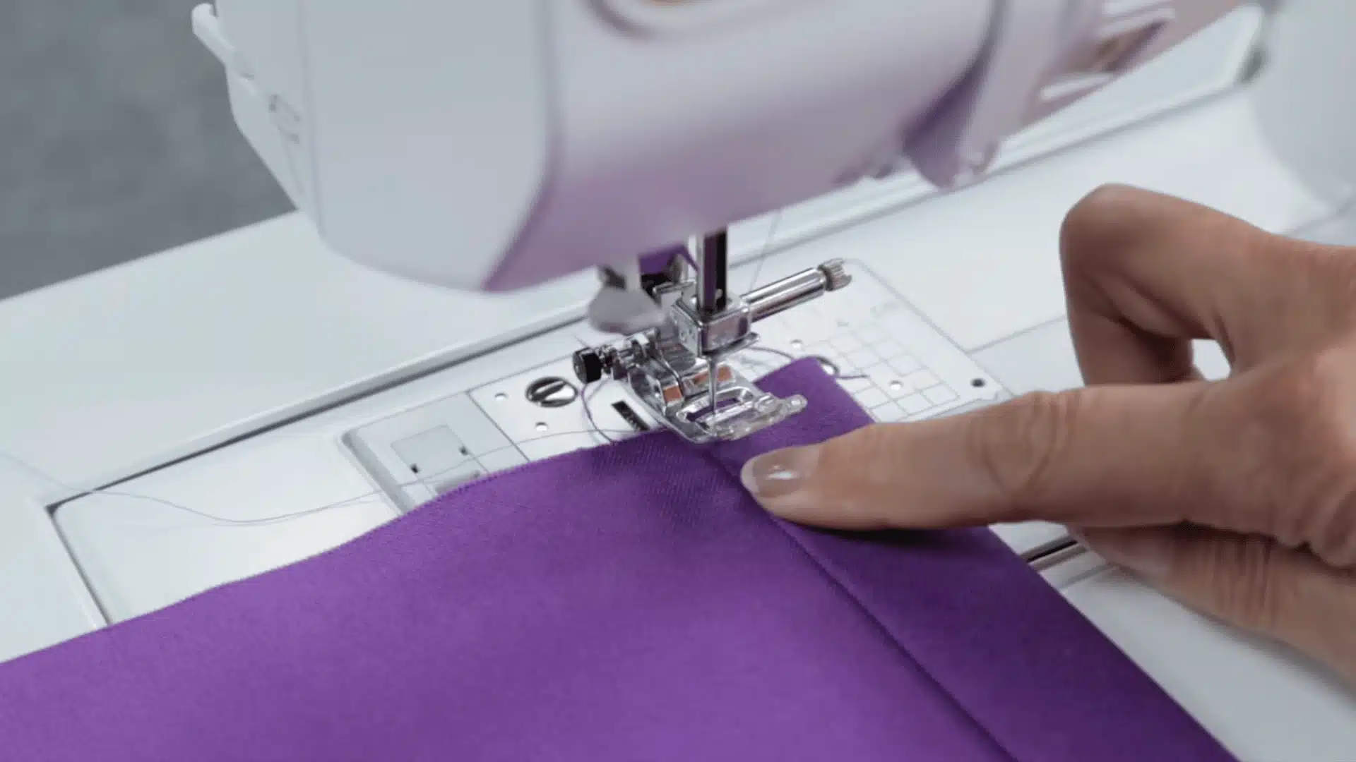 women sewing purple curtains from one end to the other end with a small machine