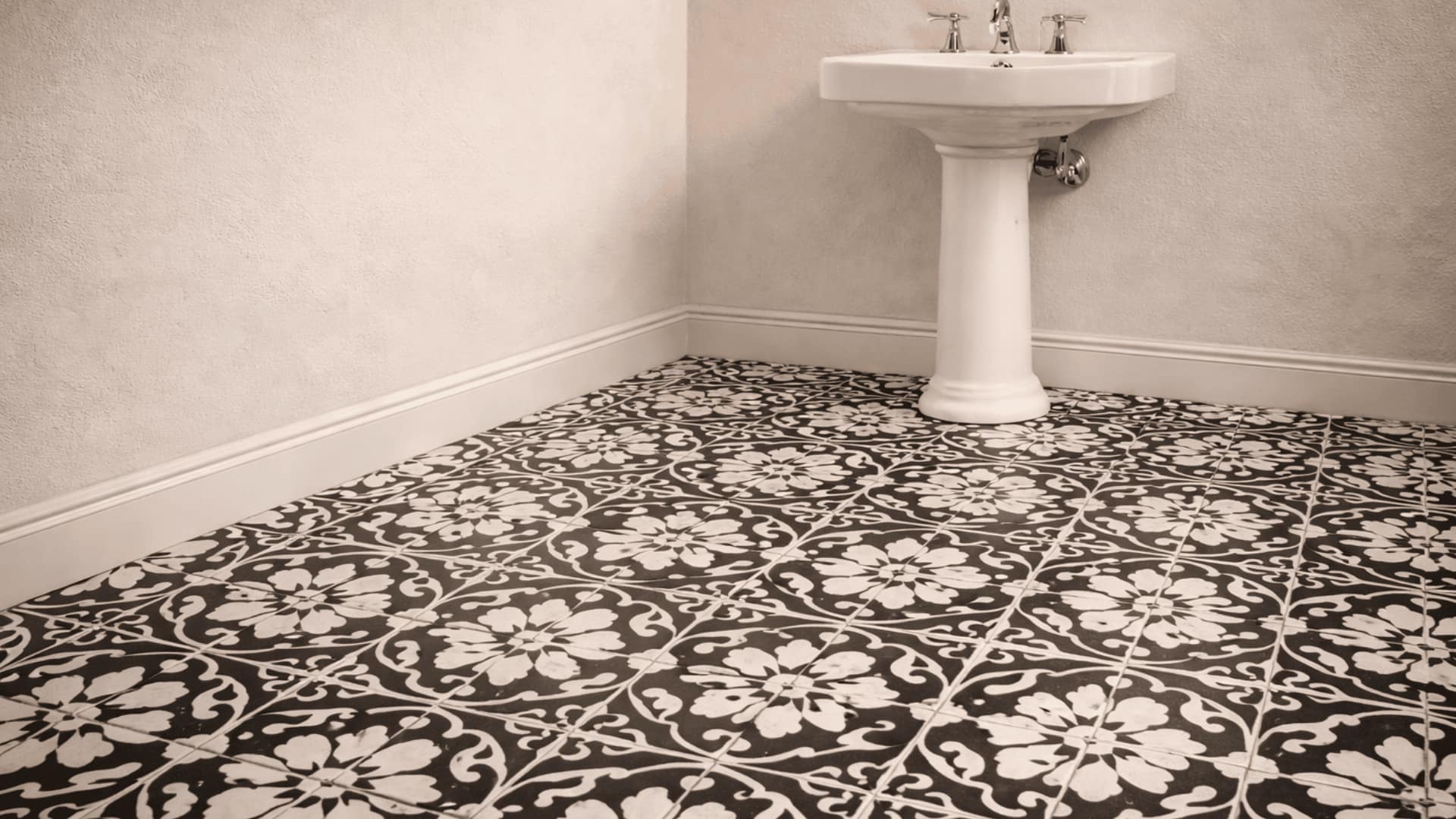bathroom floor with black and white encaustic cement tiles, floral pattern, pedestal sink and white walls