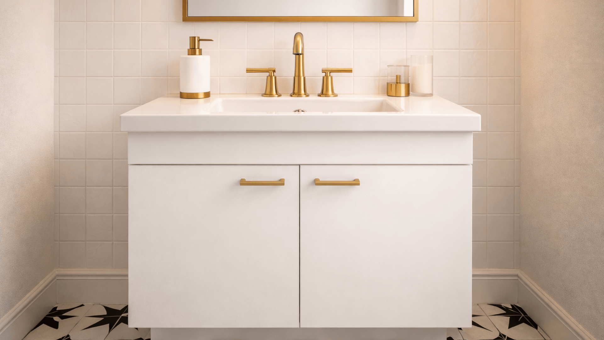 bathroom vanity with black and white geometric floor tiles, white cabinet and brushed brass faucet