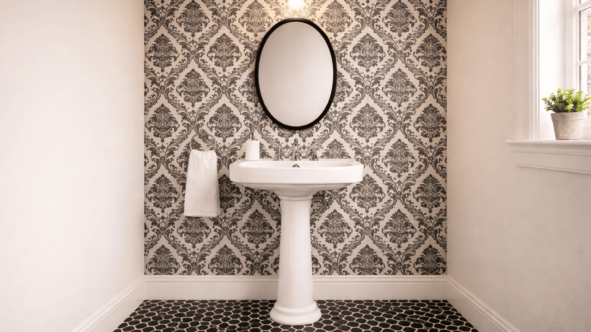 bathroom with black and white damask wallpaper, pedestal sink, oval mirror and white painted walls