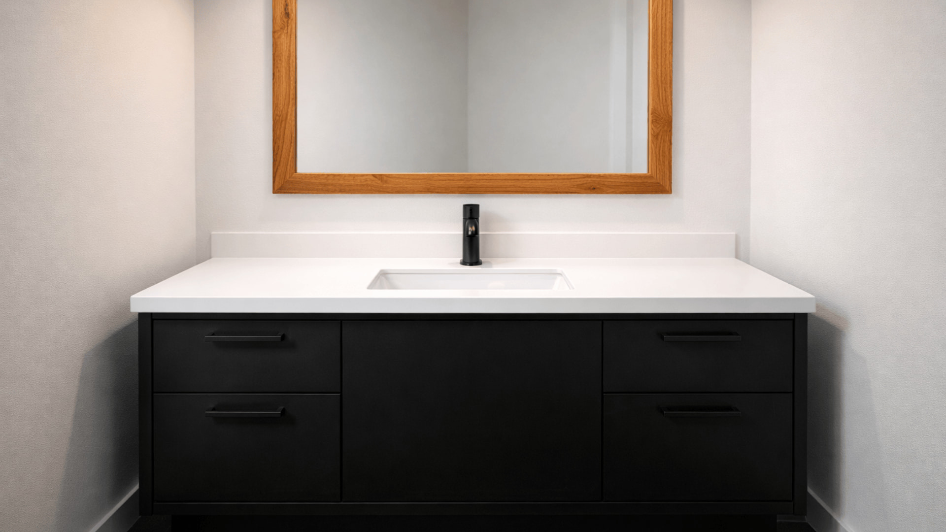 black and white bathroom with matte black vanity, white countertop, and oak framed mirror above sink