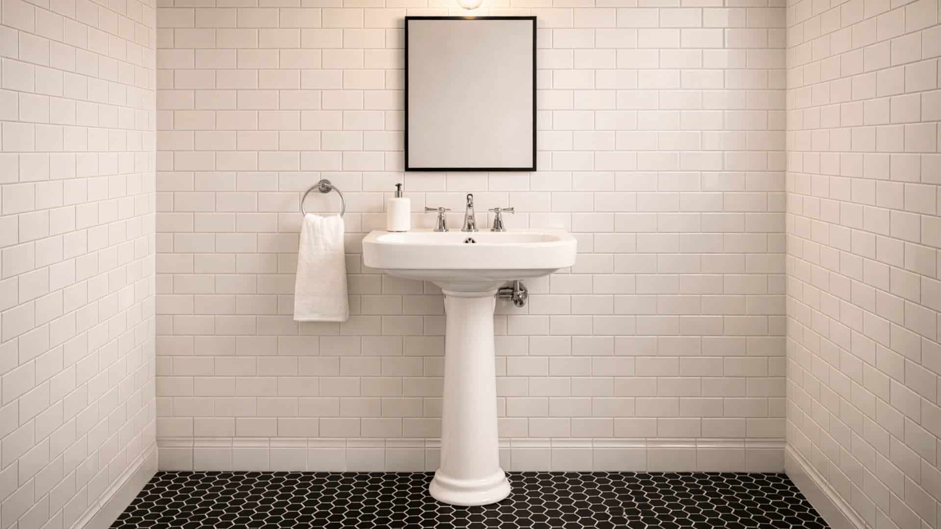 classic bathroom with white pedestal sink, black hex mosaic floor tiles, subway tile walls and black framed mirror