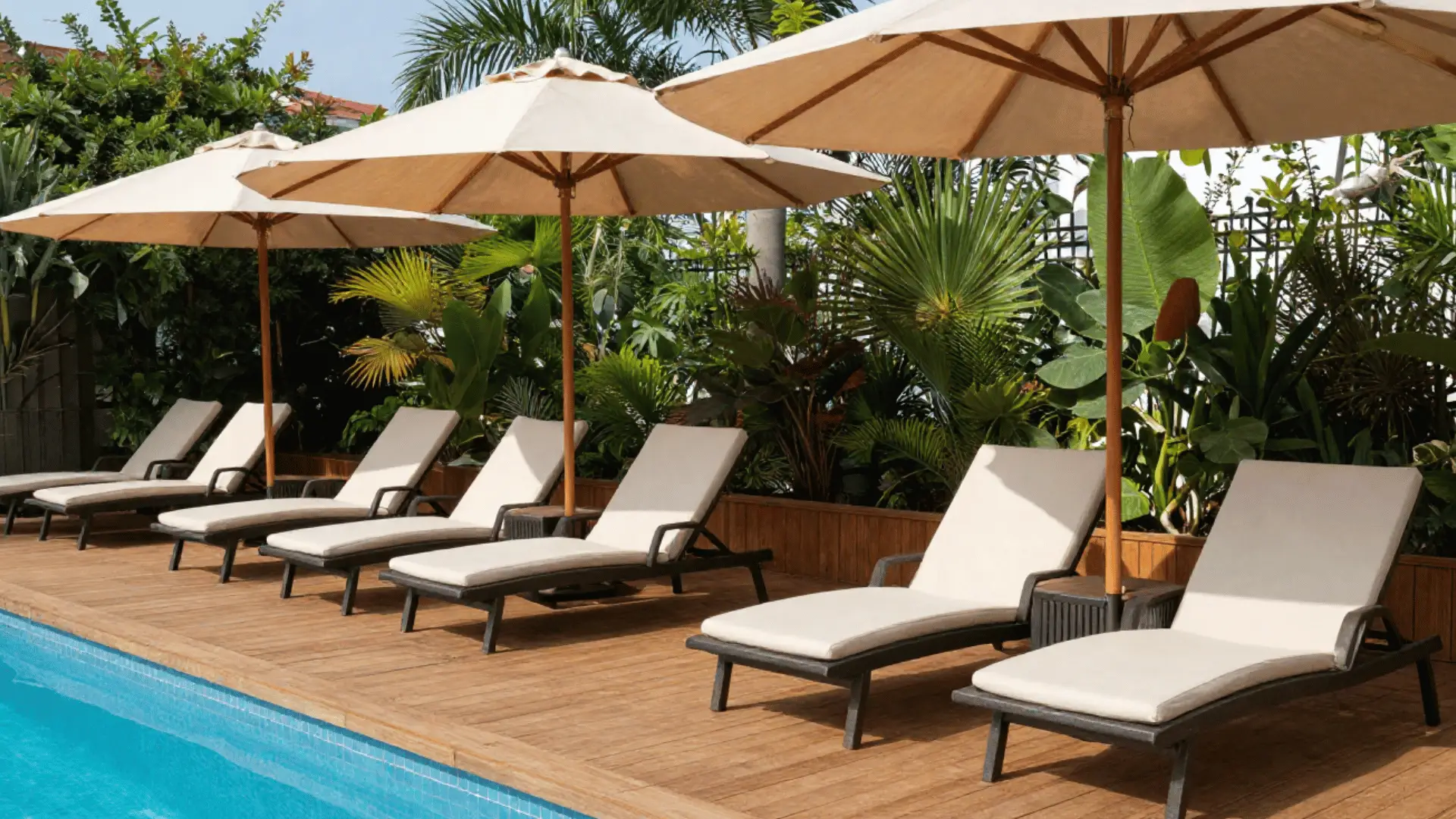 Deck poolside lounge with reclining chairs, large beige umbrellas, teak weather-resistant decking, side tables