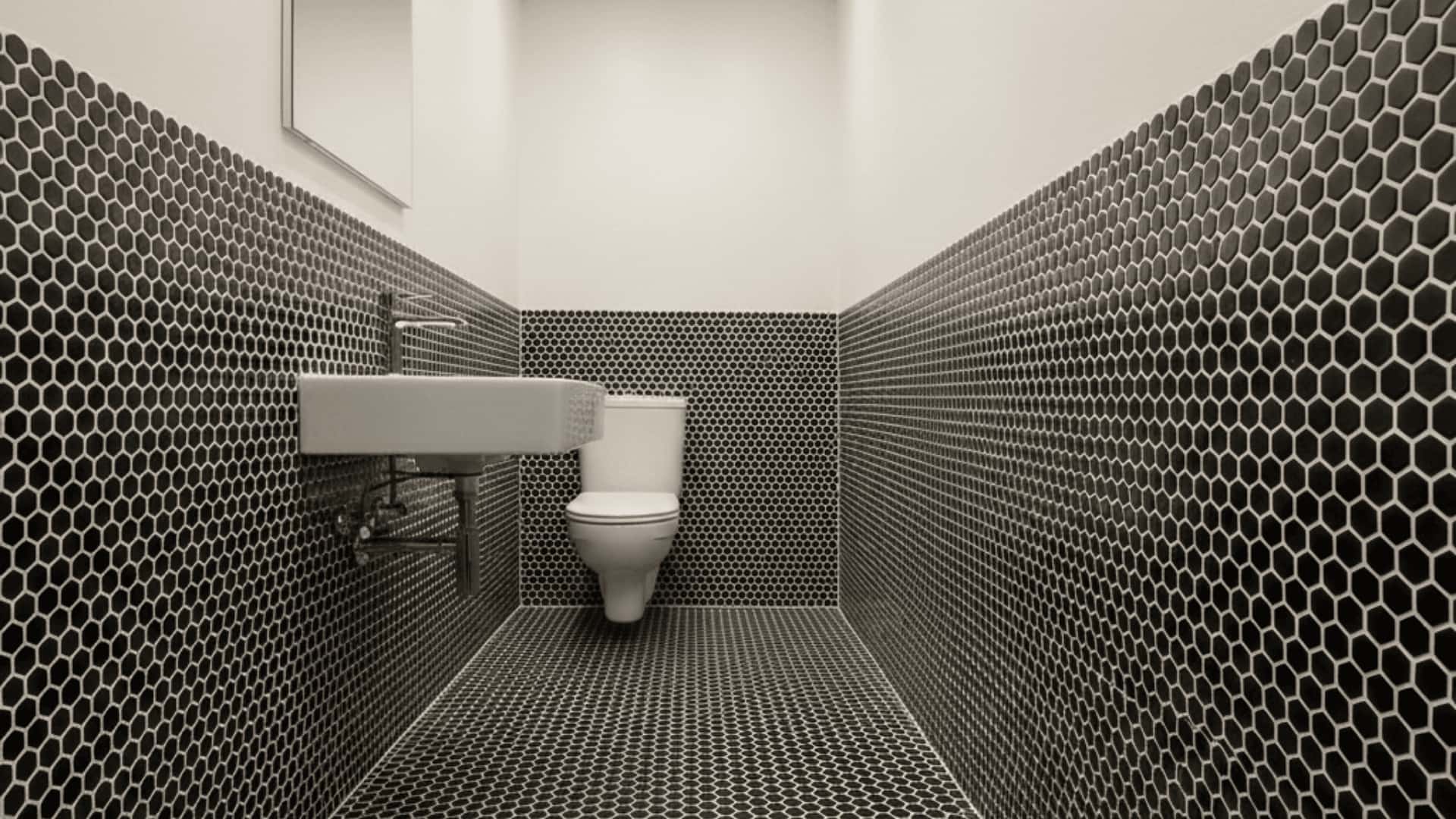 narrow bathroom with white walls, black penny tile floor, wall-mounted sink, and warm overhead lighting.