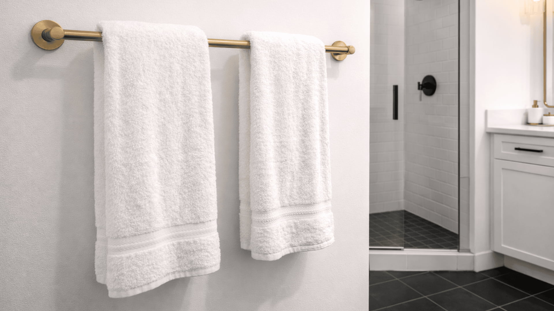 white bathroom with black floor tiles and brushed brass towel bars holding fluffy white towels