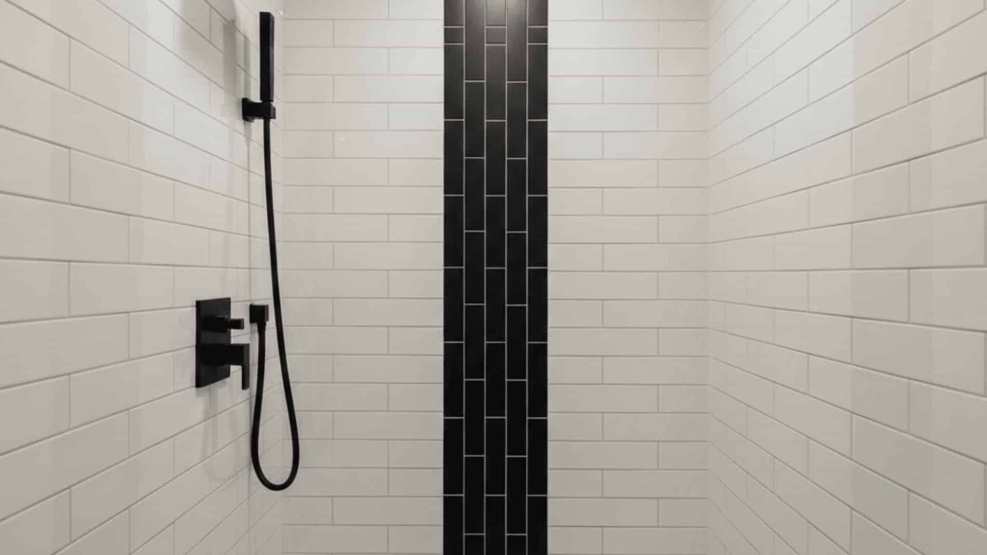 white subway tile shower with a vertical matte black tile accent, black fixtures, and overhead lighting.