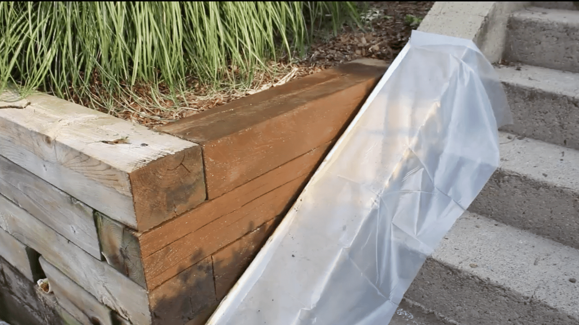 a close-up photograph of a wooden retaining wall corner with concrete steps visible on the right side