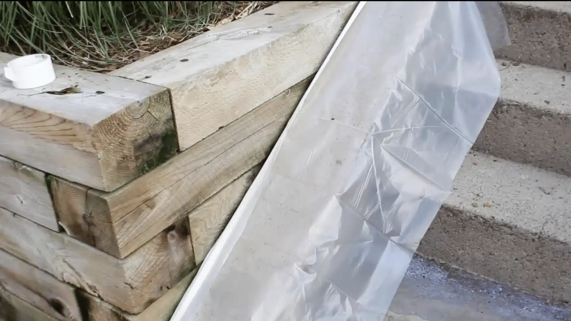 a close-up photograph of a wooden retaining wall made of rough-cut lumber blocks stacked horizontally