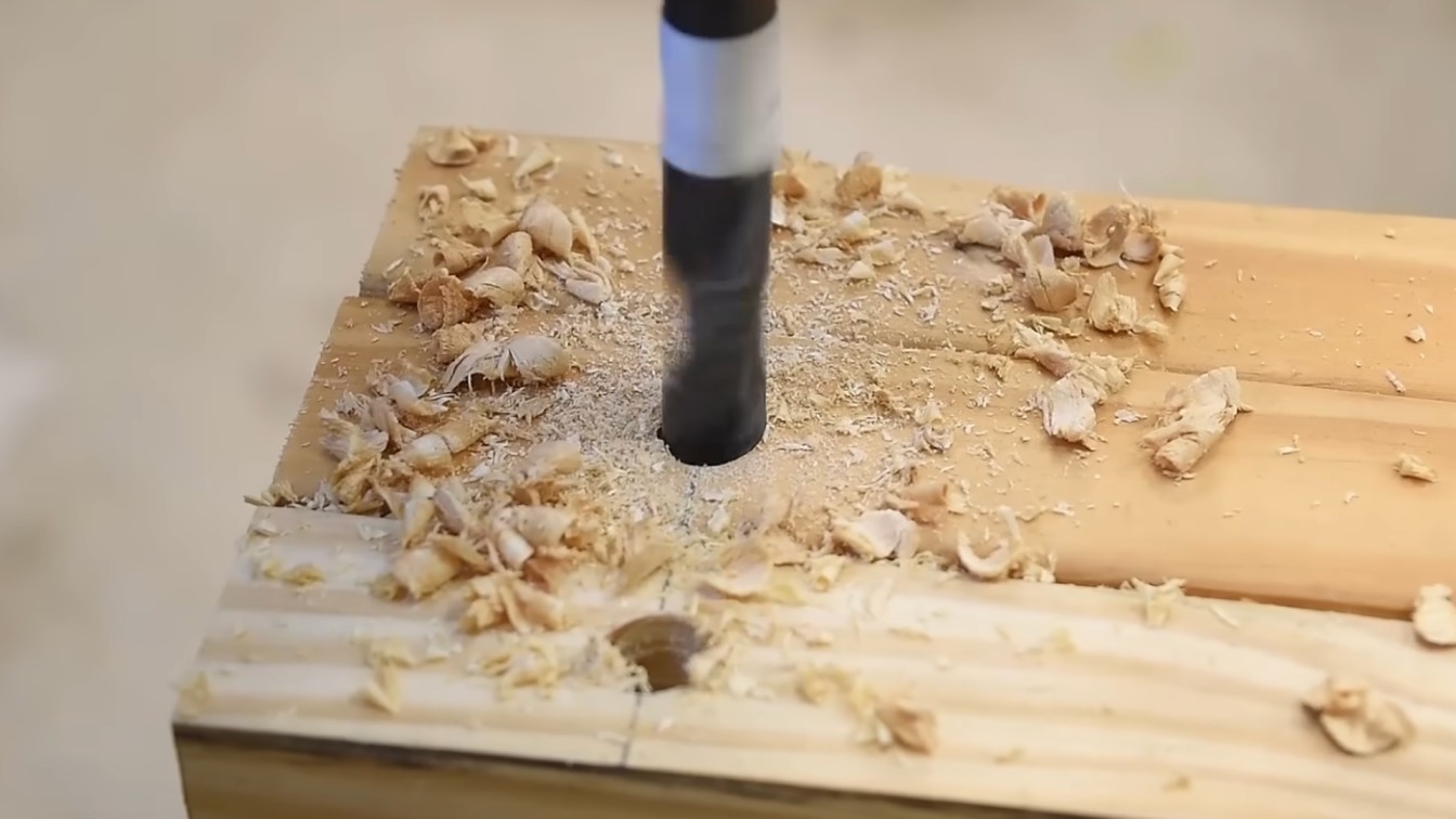 a drill bit is shown boring a hole into a wooden plank, surrounded by wood shavings and sawdust