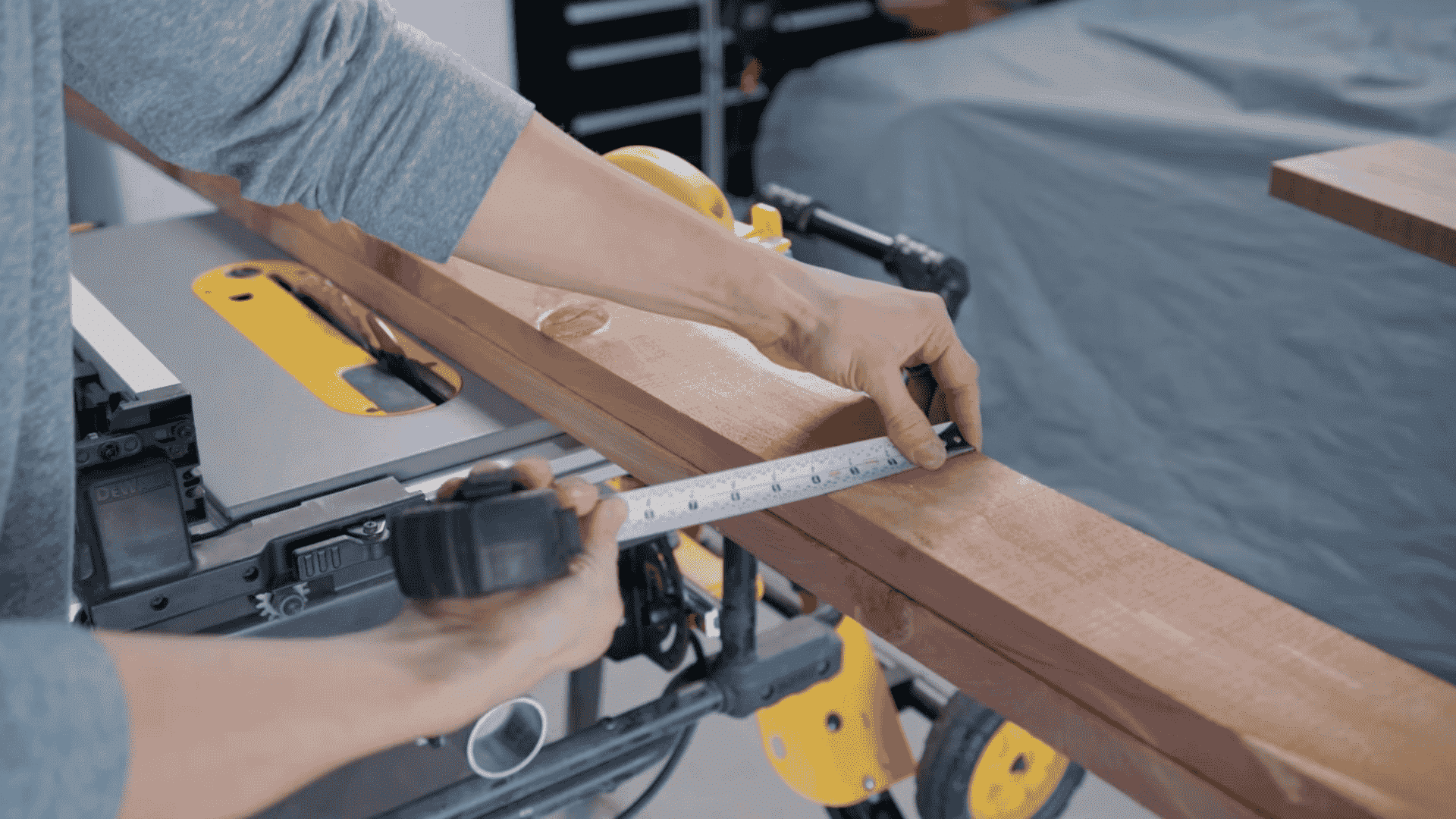 a person using a measuring tape to measure the length of a wooden board on a workbench, preparing to cut it with a table saw