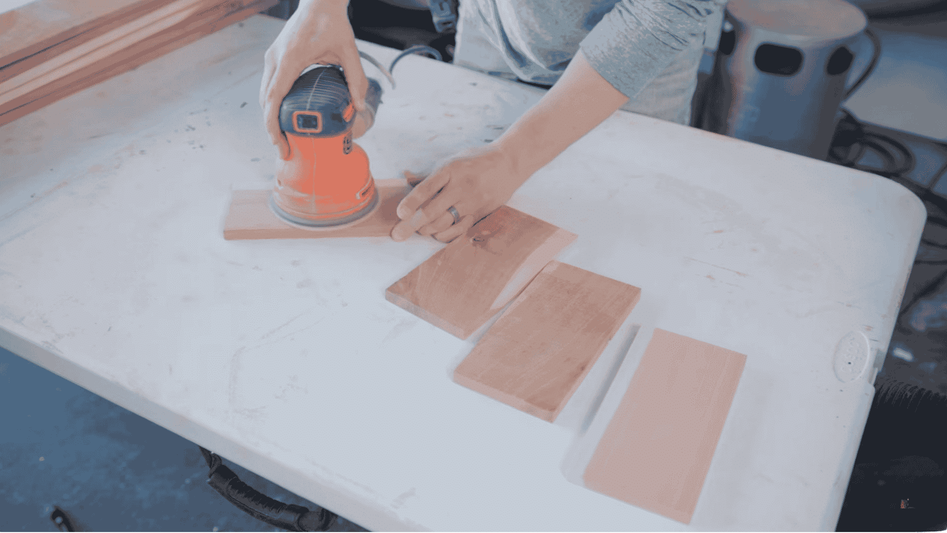a person using a power sander to smooth the surface of wooden pieces on a workbench, with several sanded wood pieces arranged nearby