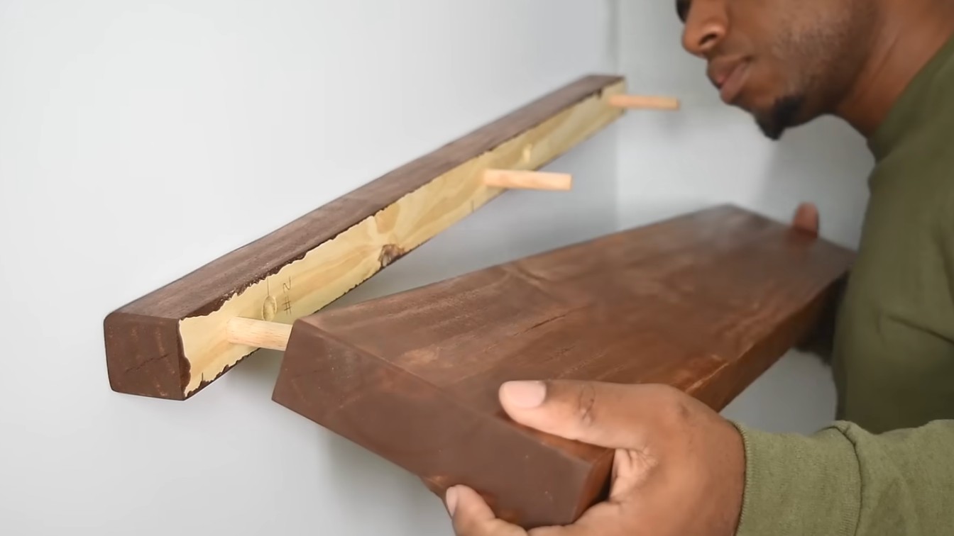 a person wearing a green shirt is mounting a wooden floating shelf onto a wall bracket