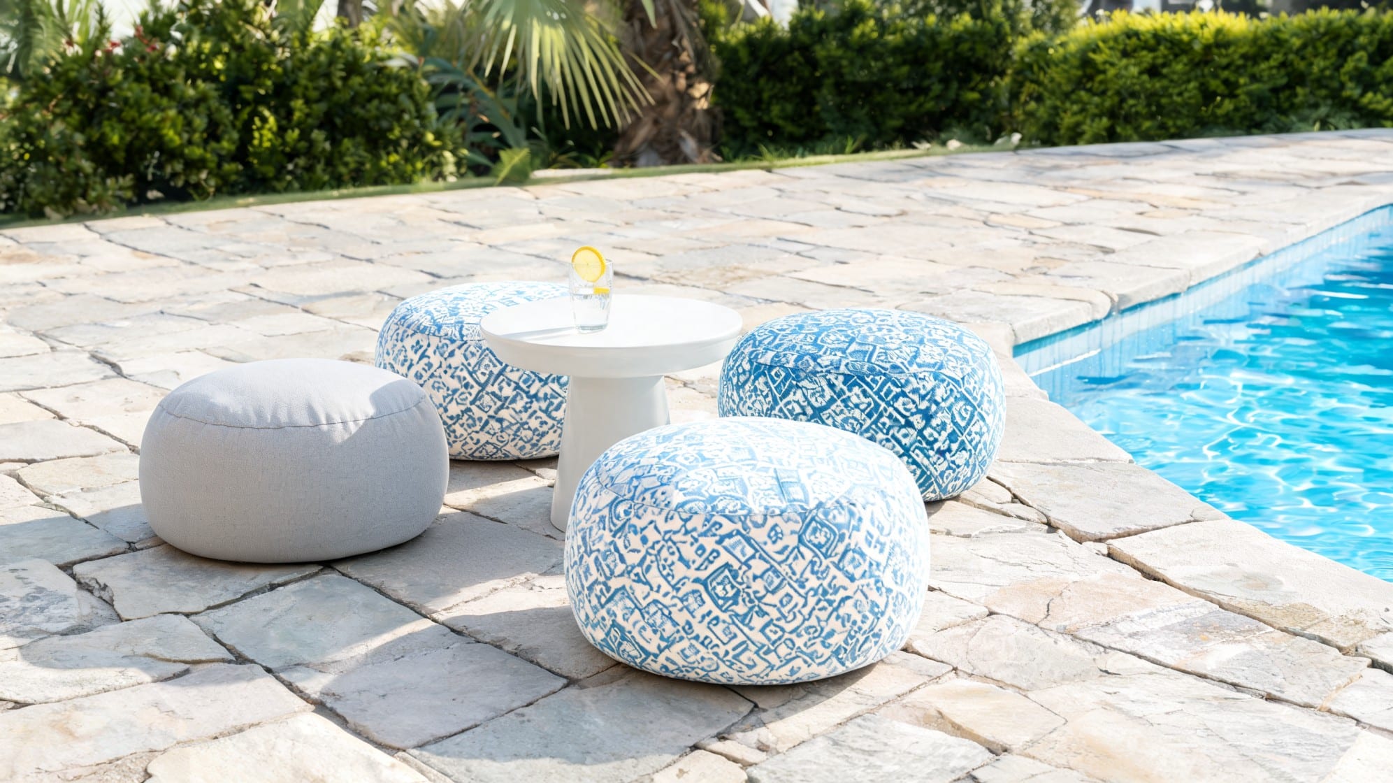 Blue and white outdoor poufs around a small white table beside a pool