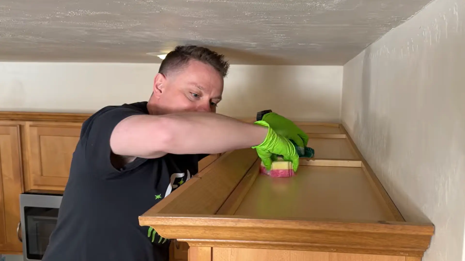 person cleaning greasy cabinet tops with a non-scratch sponge before adding a protective liner