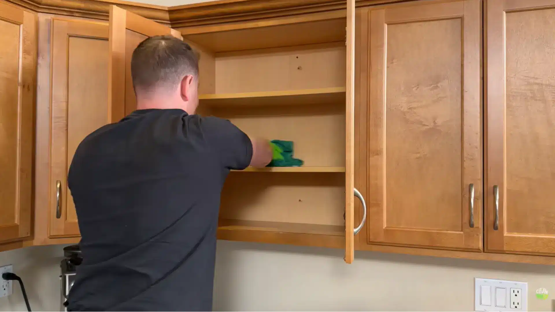 person wiping inside empty wood cabinets with a microfiber cloth during deep cabinet cleaning