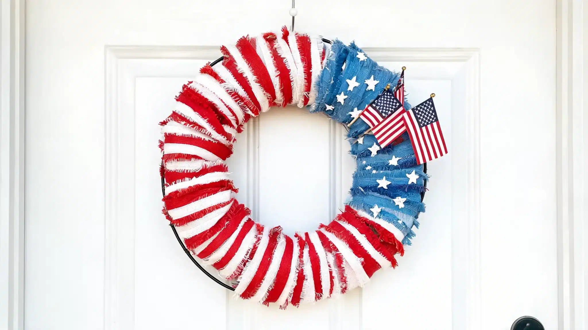 diy american flag wreath made with fabric strips, small flags, and star accents on a front door