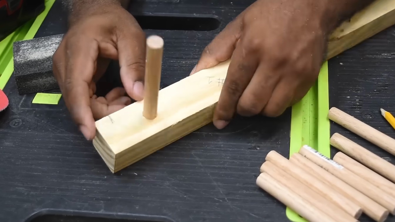 hands assembling wooden parts, placing a dowel into a rectangular block on a black surface