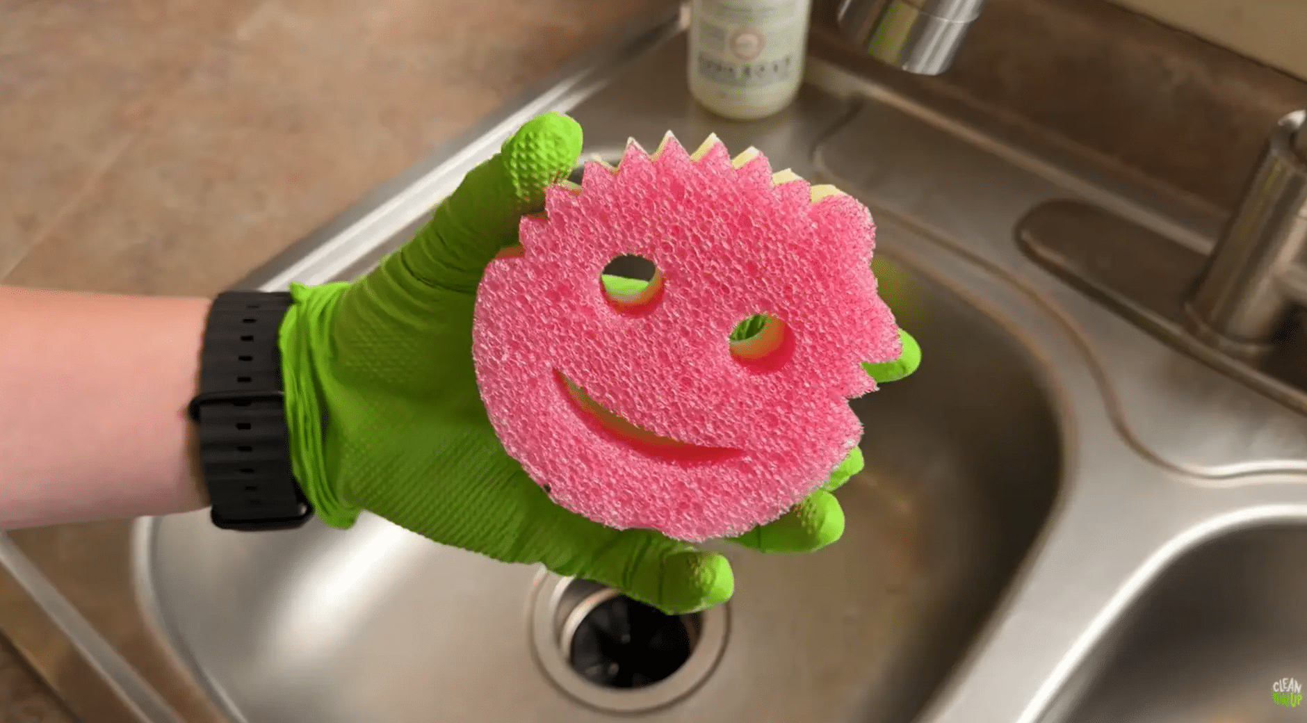 gloved hand holding a non-scratch sponge for gently cleaning tough buildup on wood cabinets