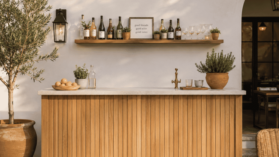 outdoor bar with wall shelf behind it holding bottles glasses plants and simple decor