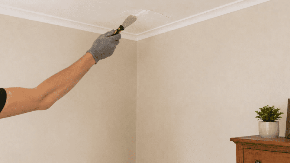 person patches damaged ceiling in the same room corner with compound and a putty knife