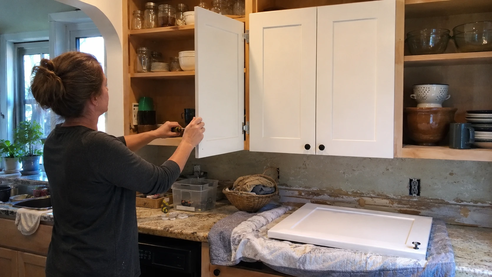 person rehanging painted kitchen cabinet door after finish has cured
