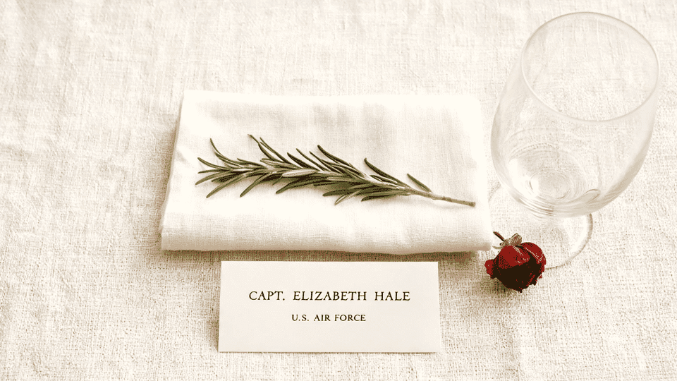 place setting with rosemary sprig handwritten card and poppy on linen table