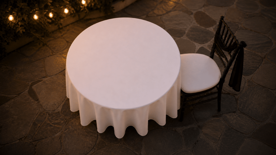 round table with white cloth and single chair pulled back with black ribbon on patio at dusk