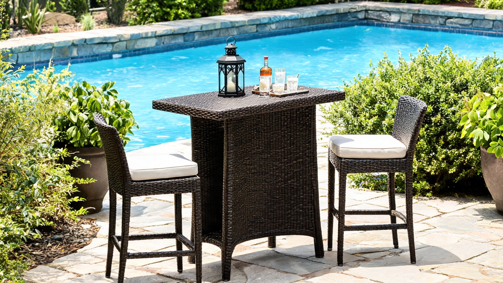 Wicker outdoor bar table with cushioned chairs beside a pool