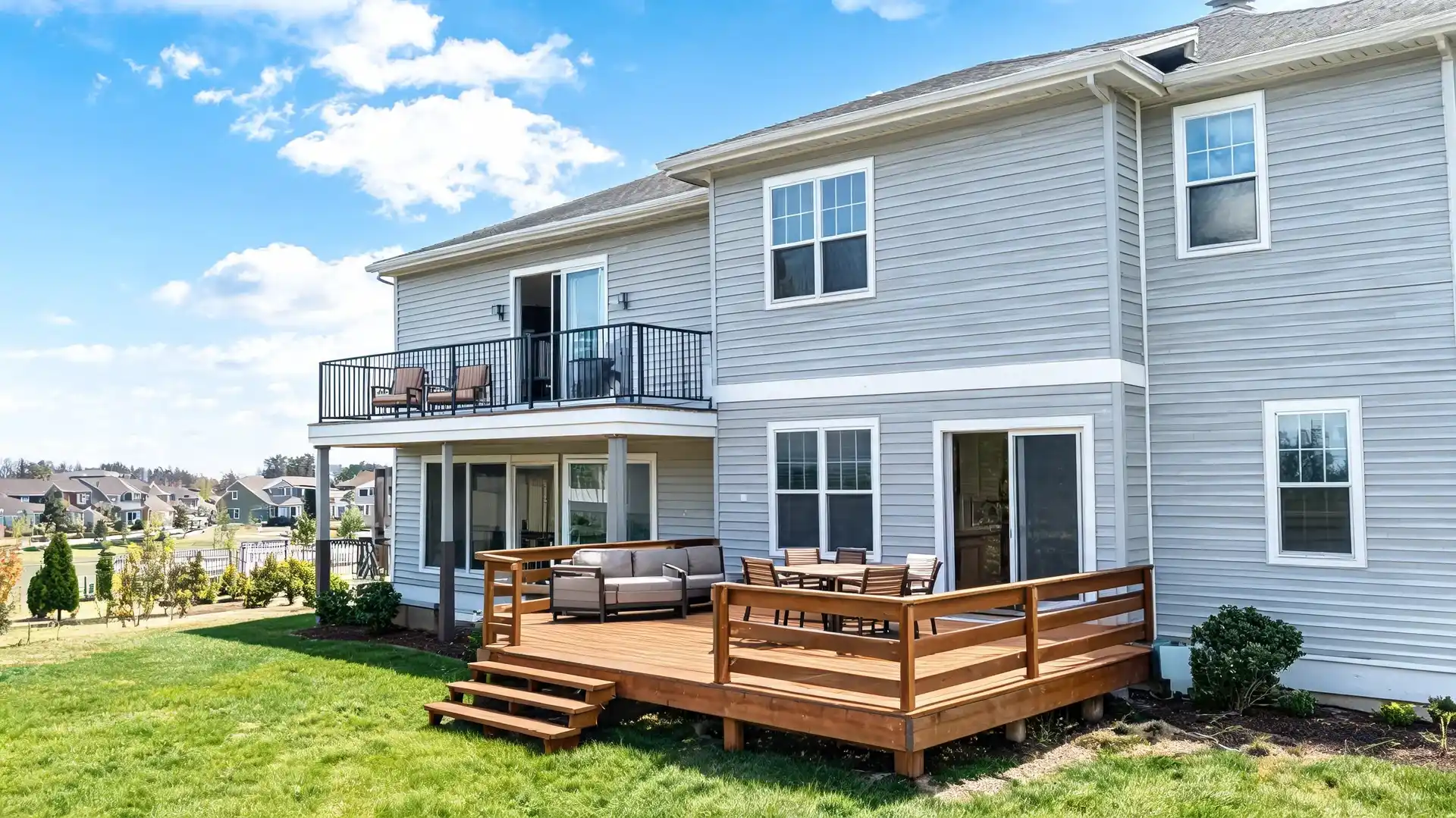 a two story house features an upper balcony and lower wooden deck with outdoor seating