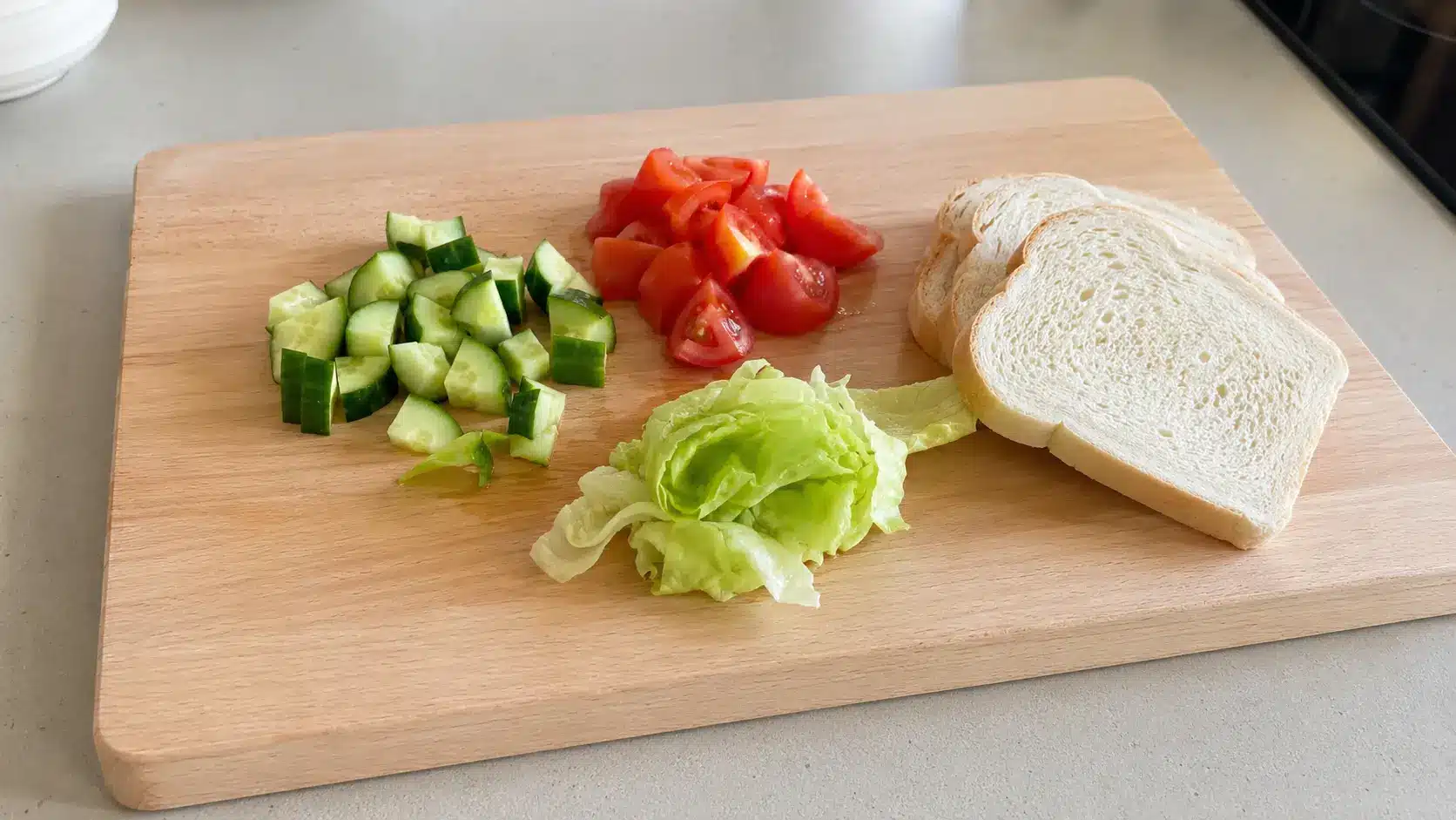 a light beech cutting board with chopped vegetables and sandwich ingredients showing a practical everyday board for simple cooking