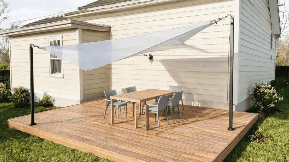 covered deck ideas on a budget with a shade sail covering a simple dining nook on a sunny wood deck