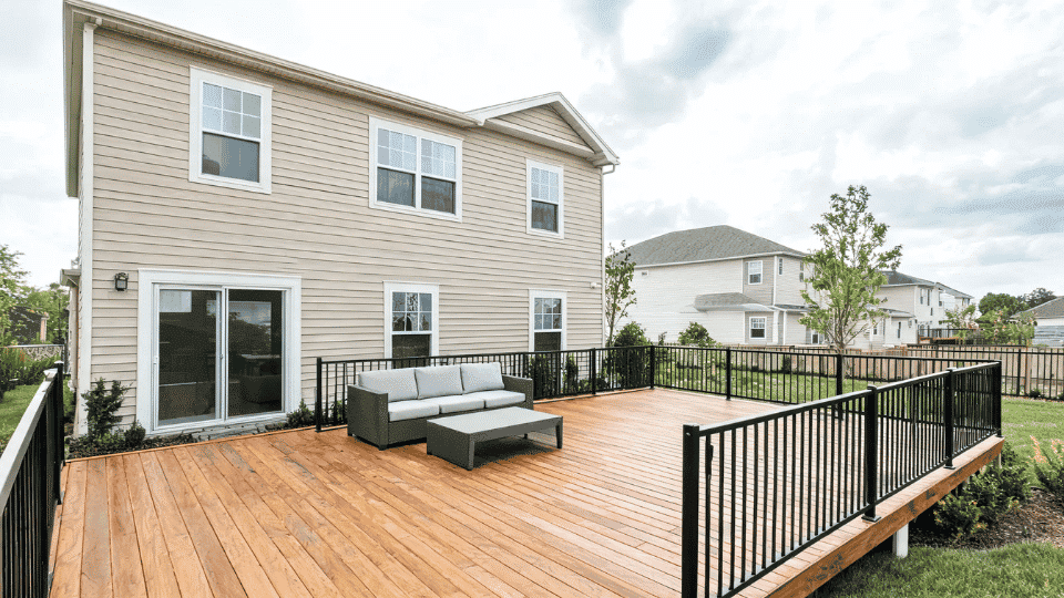 deck color ideas with natural oak boards and black metal railings on a beige suburban home