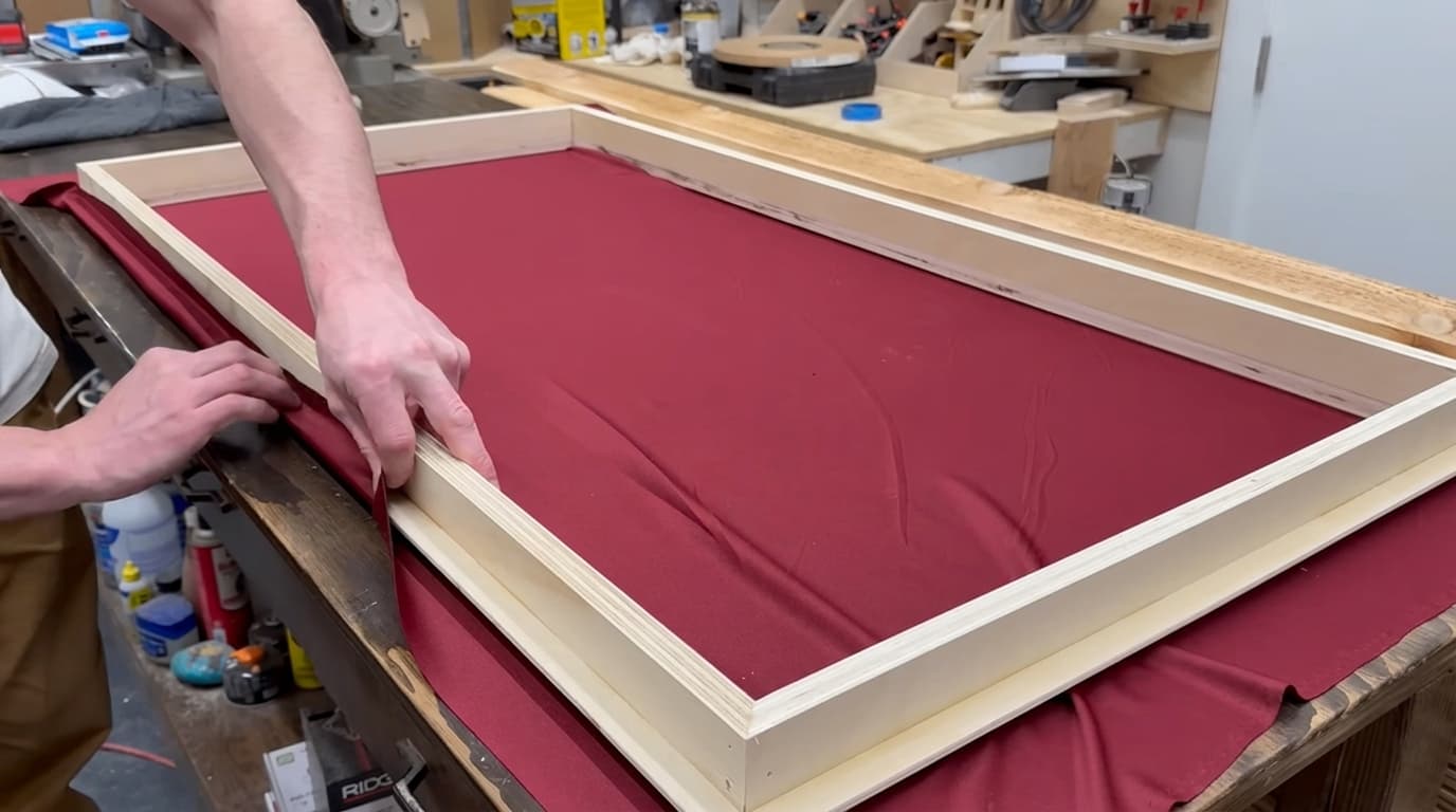 thin breathable fabric being pulled over a wooden acoustic panel frame without wrinkles