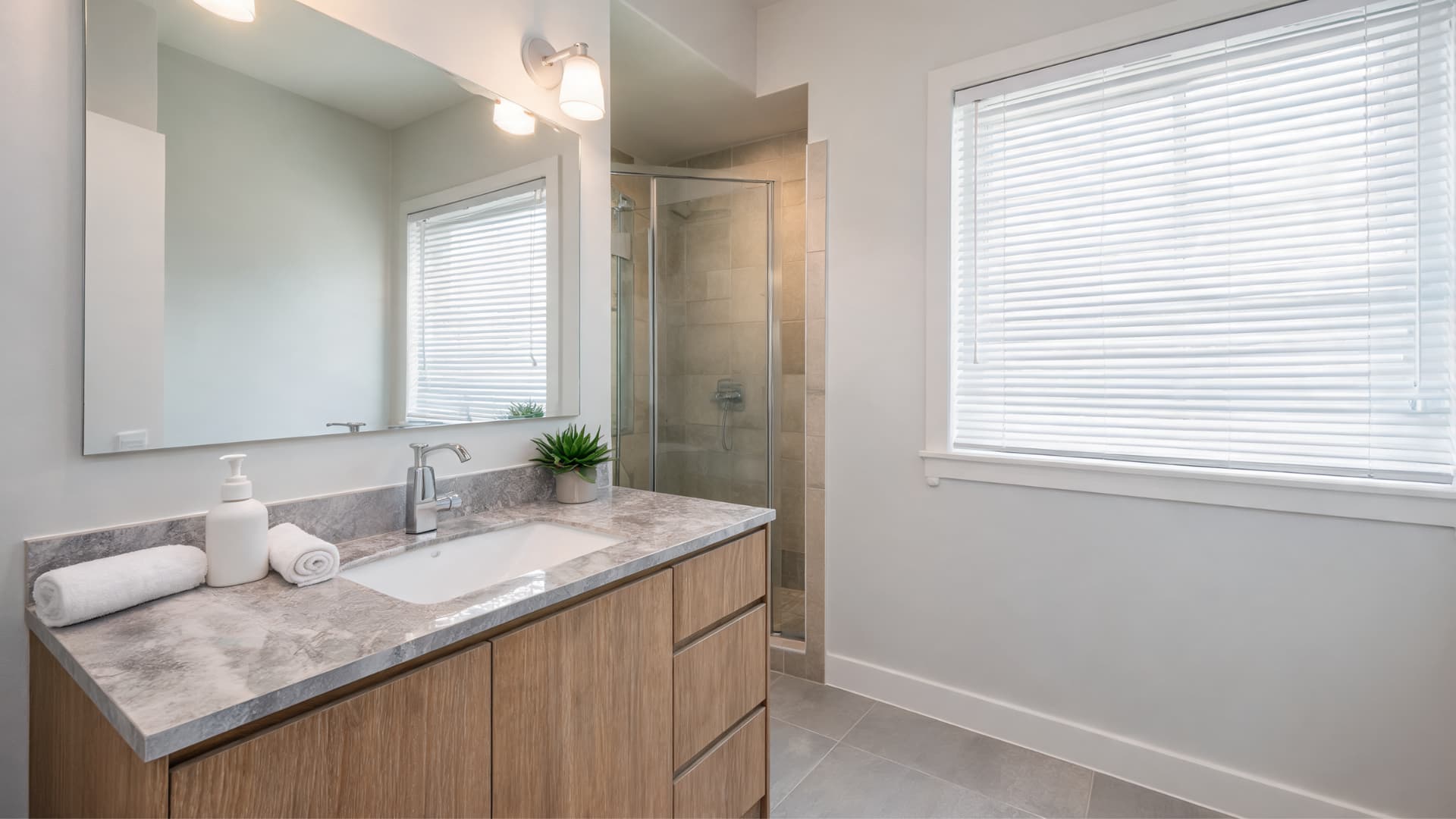 bright bathroom with eider white walls warm wood vanity gray tile and balanced natural light