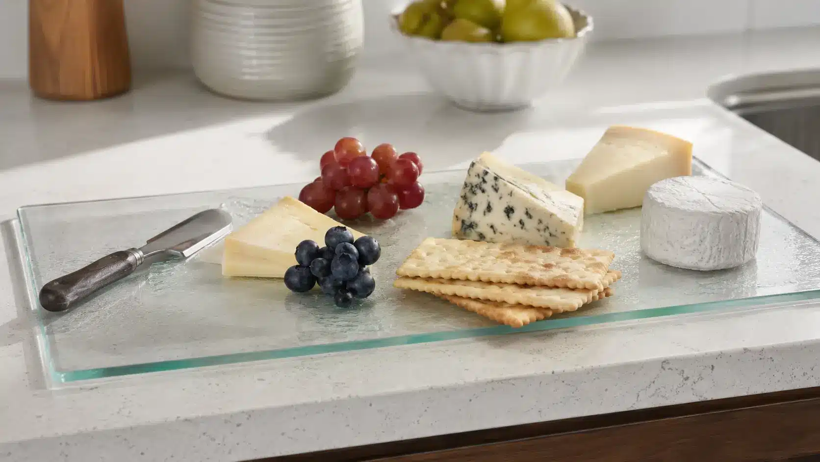 a glass cutting board used for serving cheese soft fruit and crackers showing it as a light slicing and serving board instead of a daily chopping board