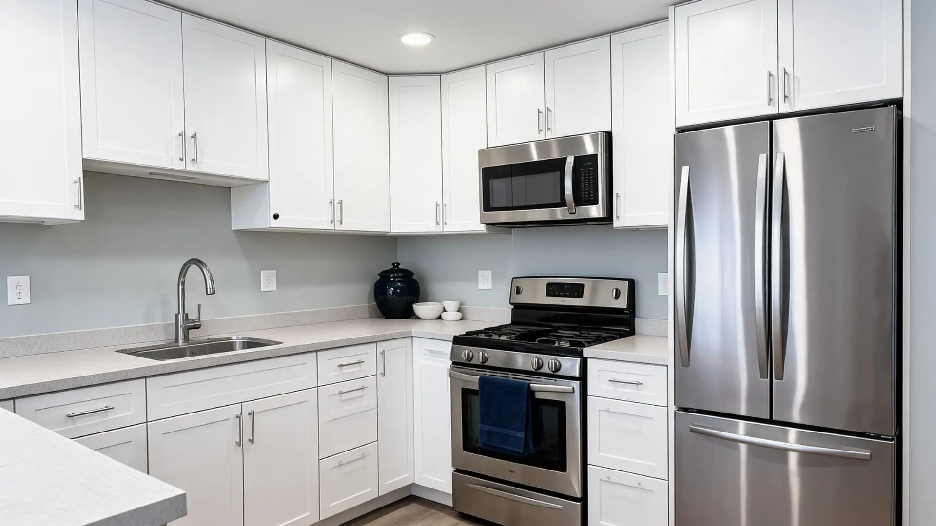 kitchen with Benjamin Moore Gray Owl-inspired light gray walls, white cabinets, quartz counters, stainless steel appliances, and chrome fixtures
