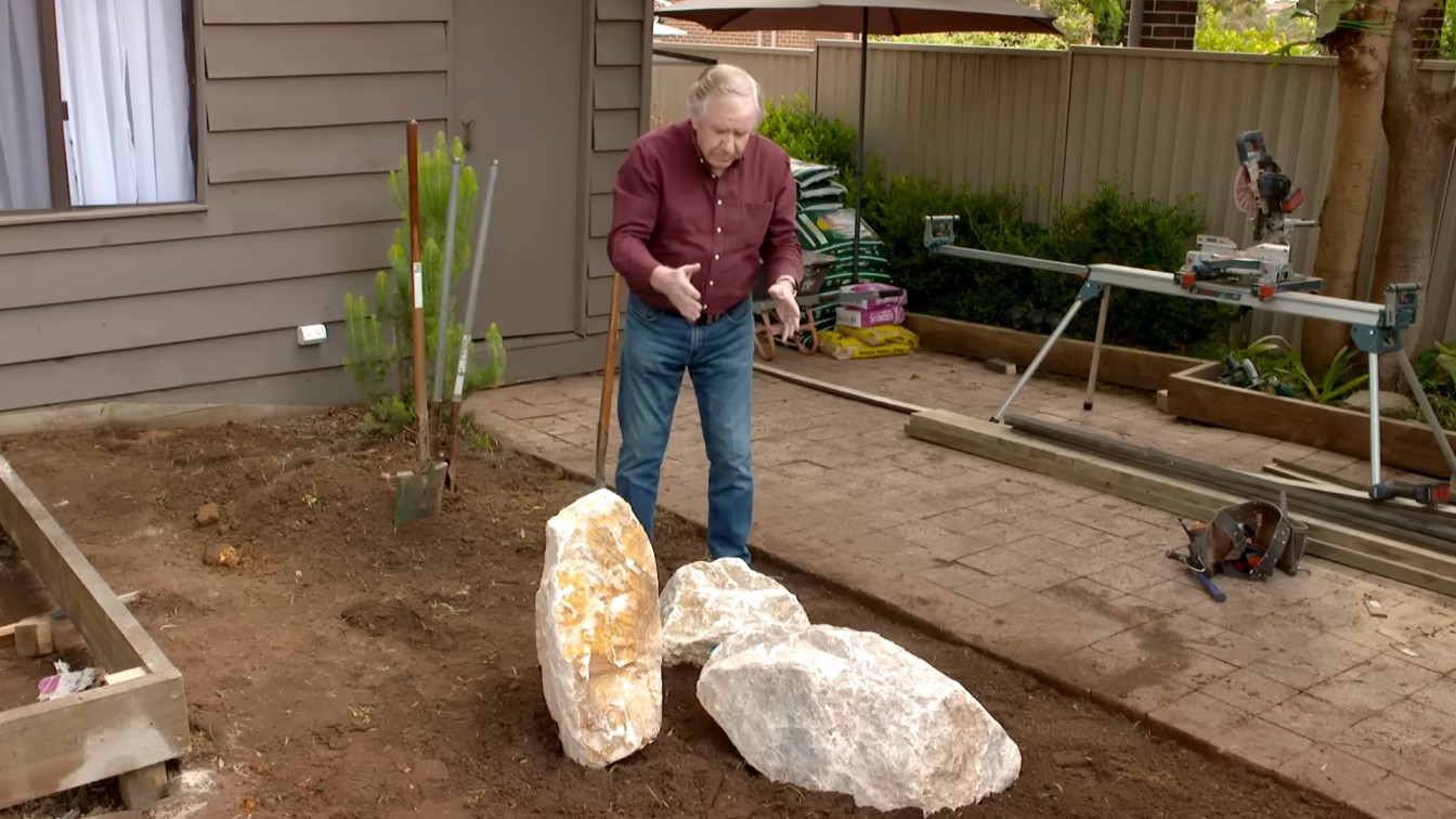 landscape designer standing near large feature rocks and garden tools in a backyard makeover