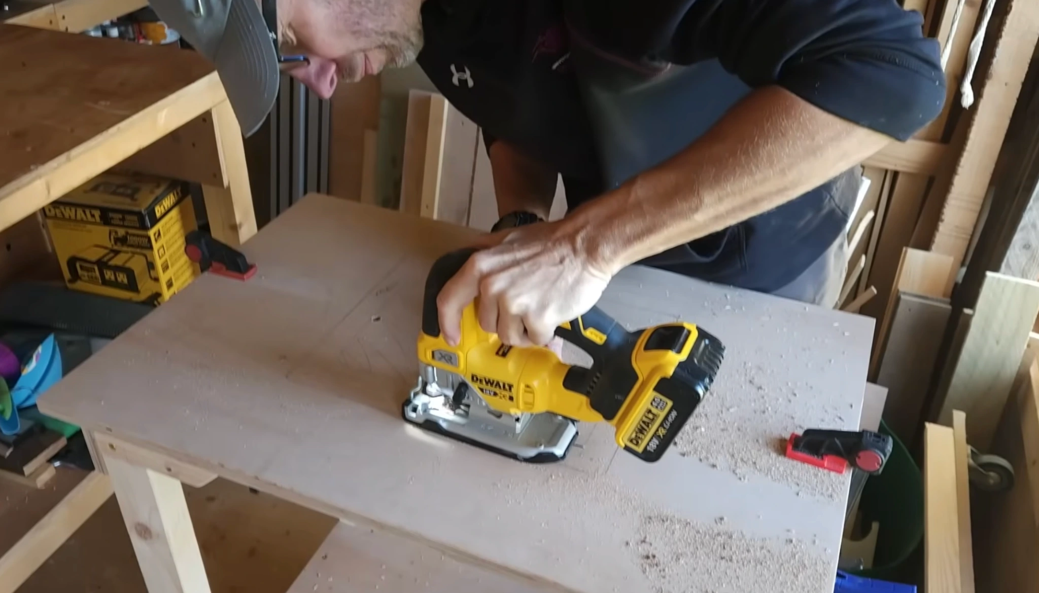 man using a cordless jigsaw to cut the router table top in a workshop with wooden pieces and tools around