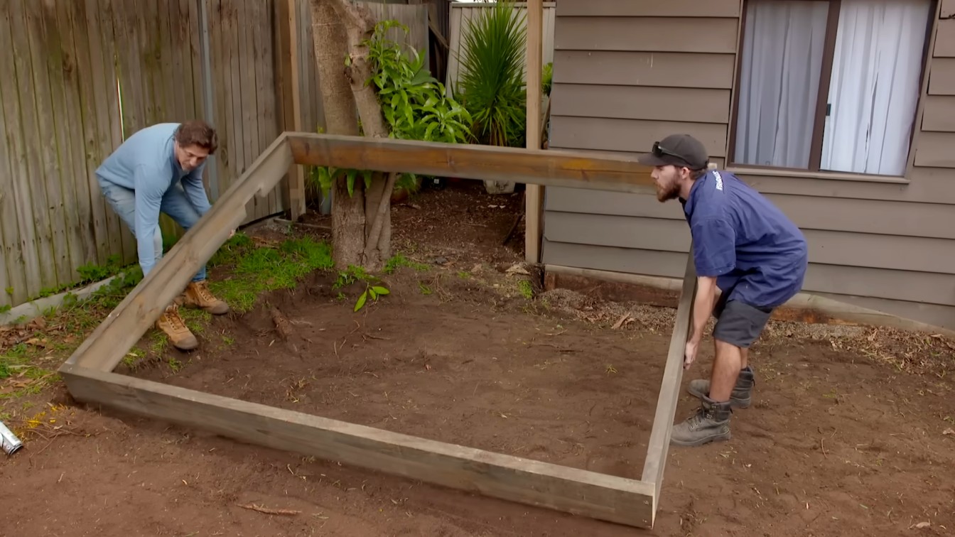 two landscapers building a timber garden border around a backyard planting area near a house