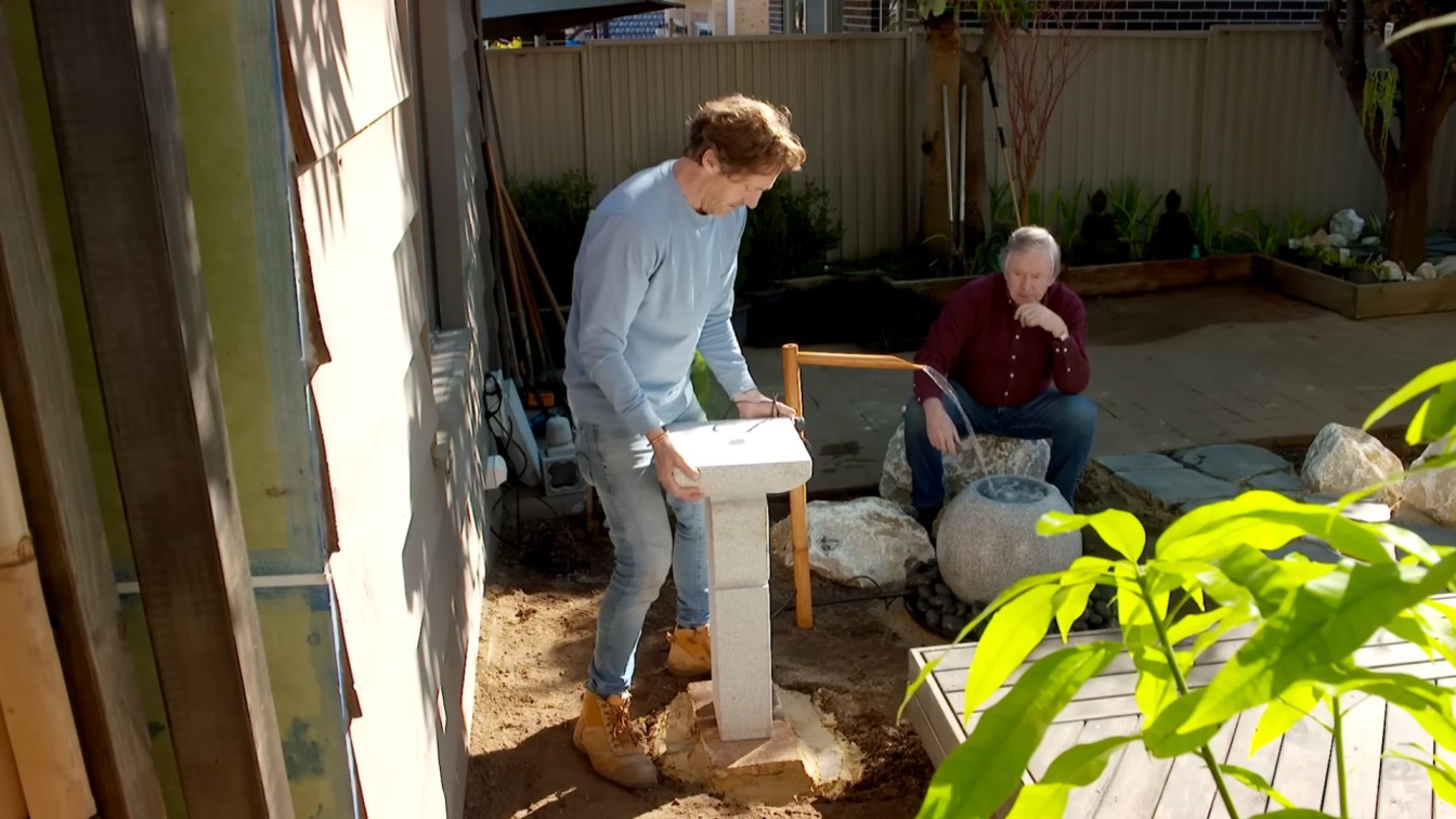 two people installing a small garden feature beside rocks during a backyard landscape makeover
